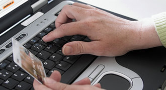 Un usuario escribe en un teclado y sostiene una tarjeta bancaria