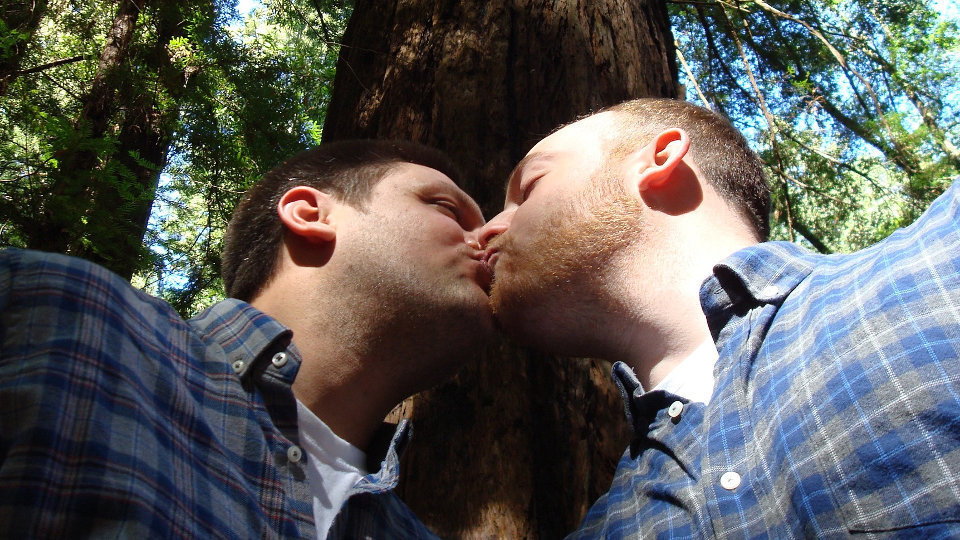 Dos hombres se besan bajo un árbol. AEP
