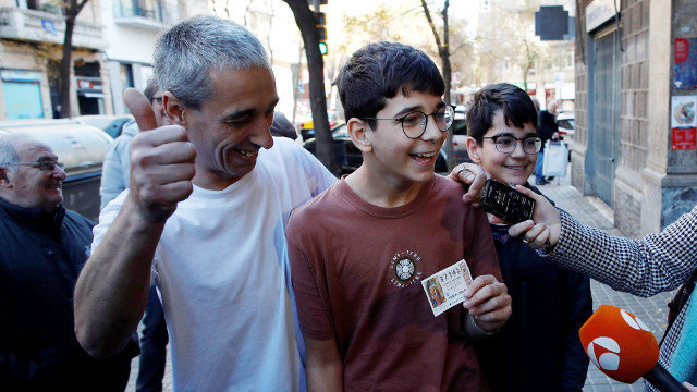 Cosmin.C., acompañado do seu pai, mostra o seu décimo agraciado co premio da loteria do Neno. ALEJANDRO GARCÑIA (EFE)
