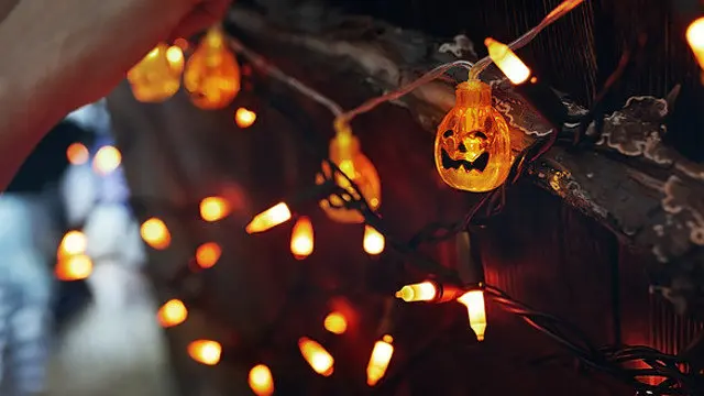 Woman hanging decorative eletric light with pumpkins. Halloween theme