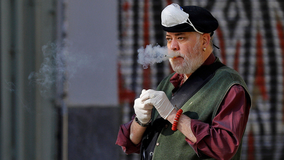 Un hombre fumando con guantes y una mascarilla en la cabeza. EFE