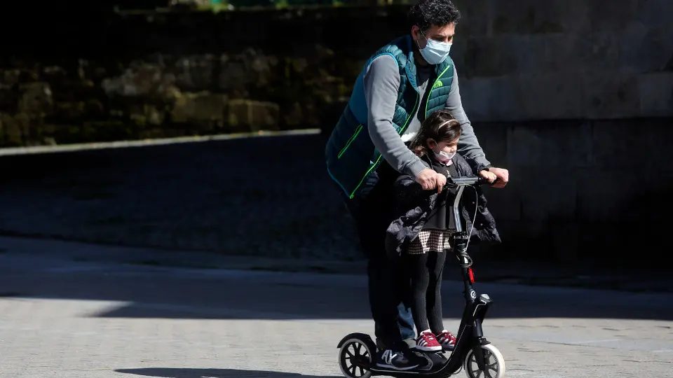 Un hombre y una niña con mascarilla en un patinete. ADP