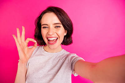 Self portrait of charming, cheerful attractive nice cute girlfriend showing you ok sign taking selfie wearing grey t-shirt assessing joke quality while isolated with fuchsia bright color background