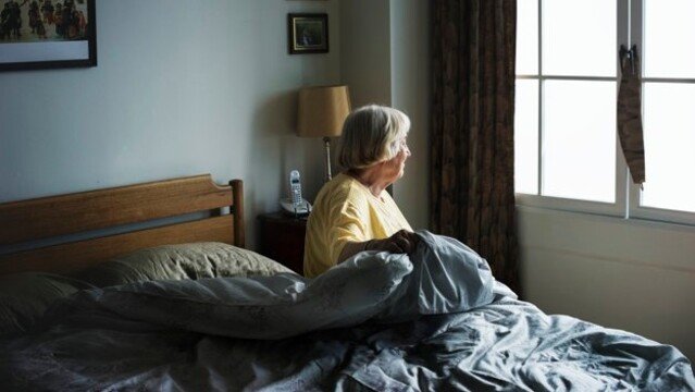 Mujer mayor sentada en una cama de residencia