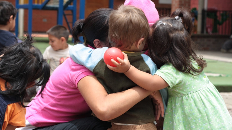 Varios niños abrazados a su profesora en el patio de un colegio. CEDIDA