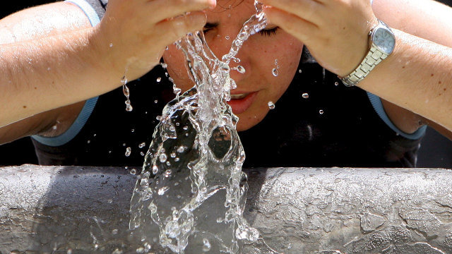 Una mujer se refresca con agua de una fuente. AEP