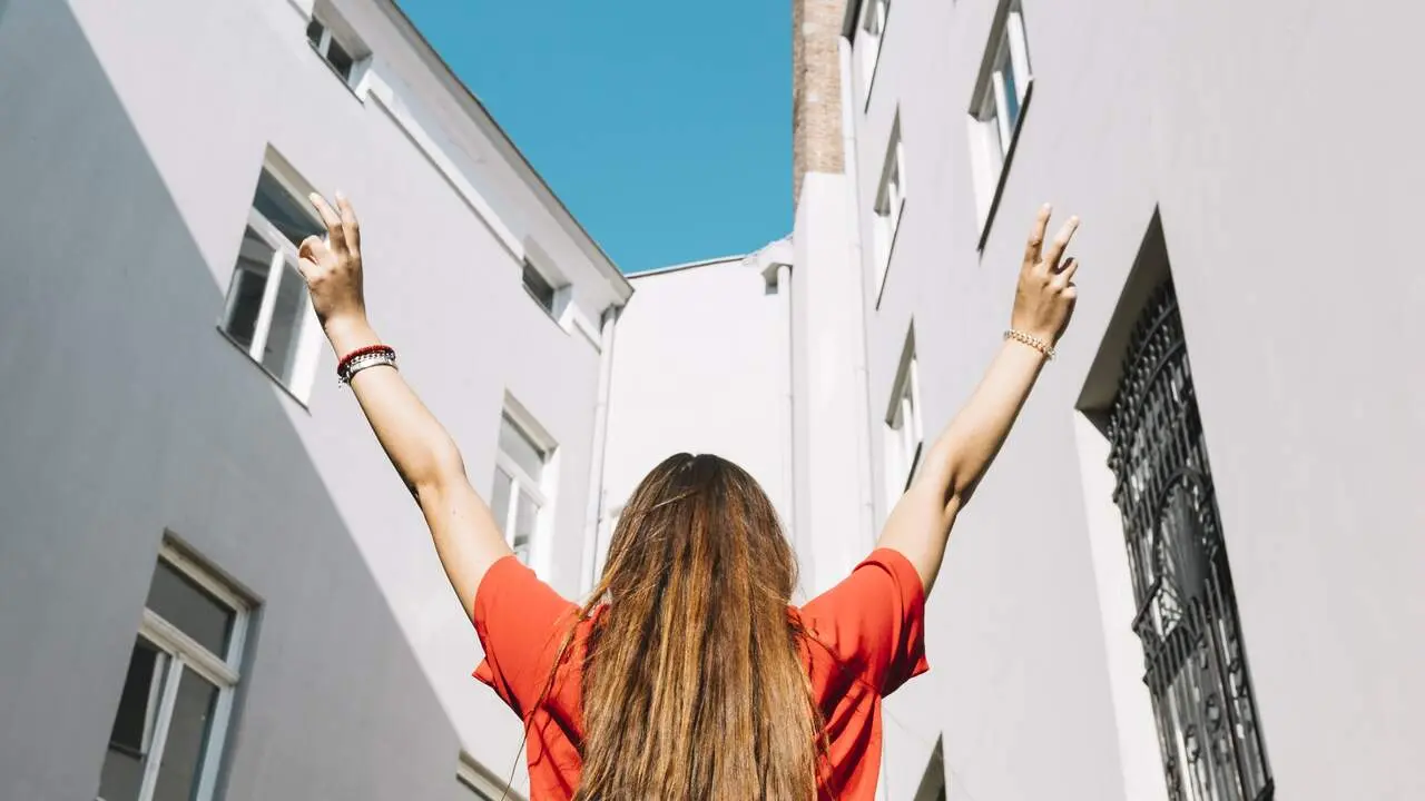 Una joven ante un bloque de viviendas. FREEPIK.