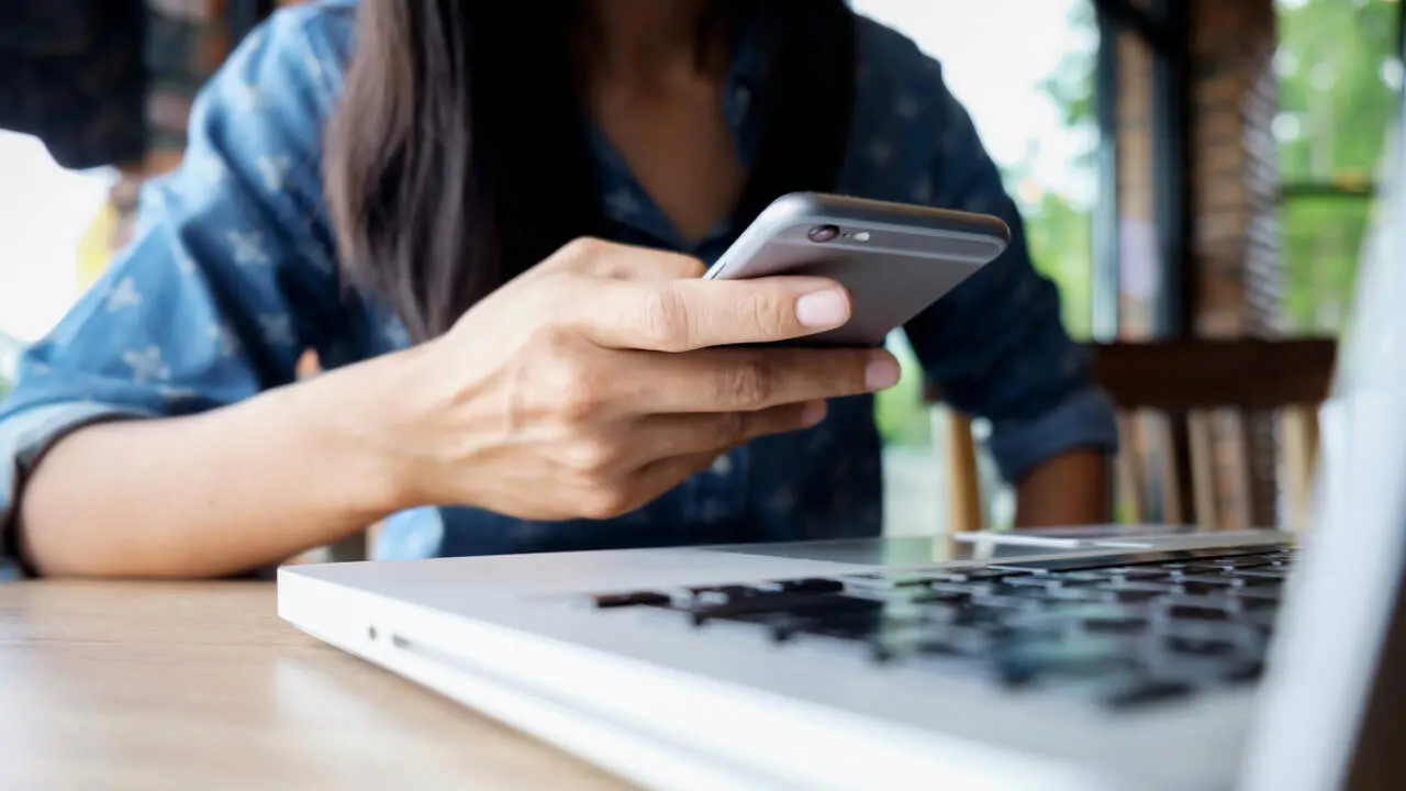 Una persona con su m&oacute;vil ante un ordenador. FREEPICK