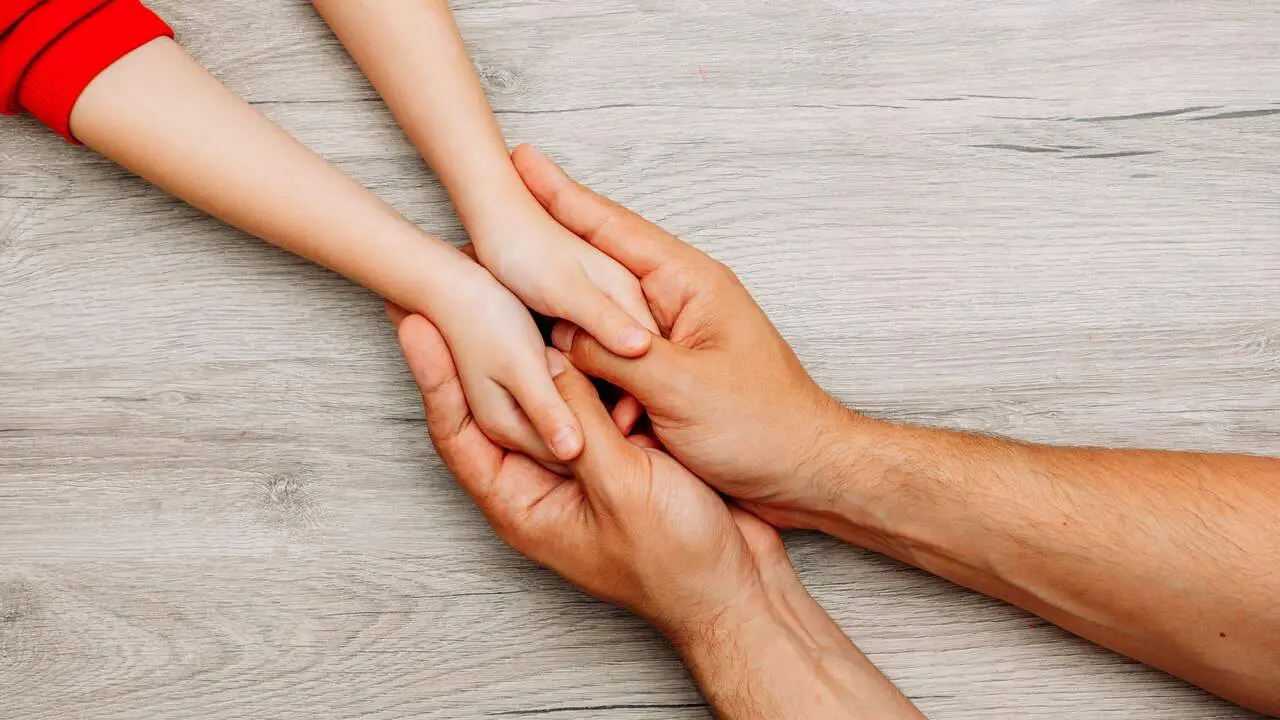 Persona adulta sujetando las manos de un menor. FREEPIK