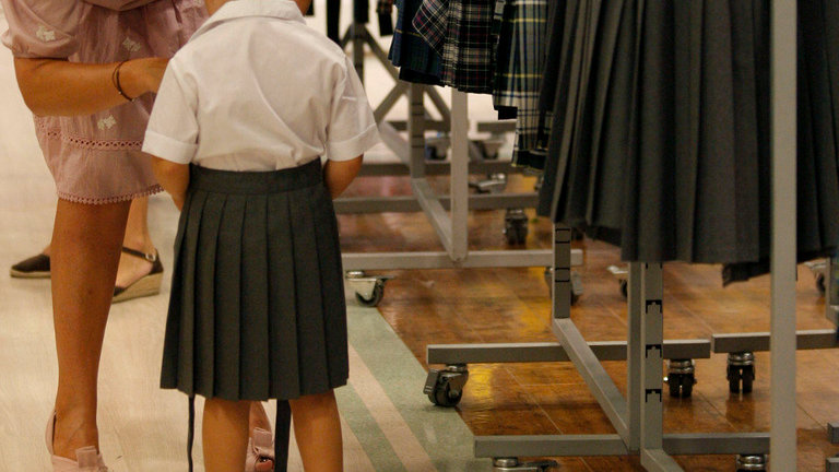 Una mujer toma las medidas a una niña para confeccionar la falda de su uniforma escolar. AEP