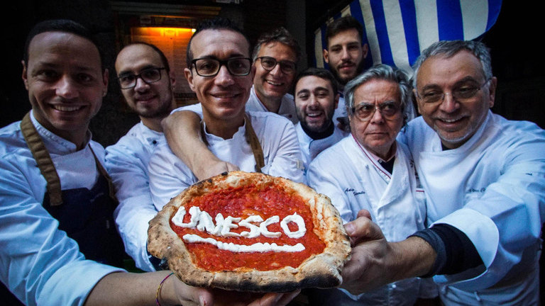 Pizzeros celebran el reconocimiento de la Unesco mientras posan con una pizza en Nápoles. CESARE ABBATE (EFE)