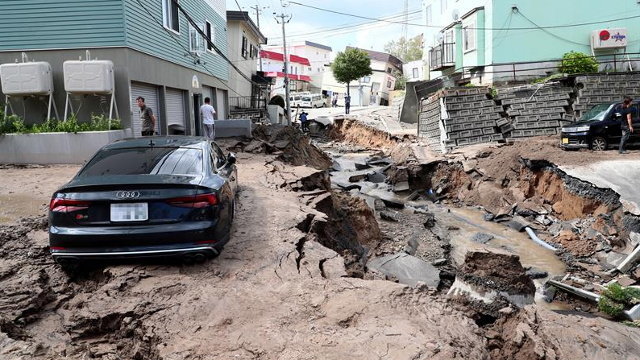 Un vehículo permanece atrapado entre el lodo en una calle destruida por el terremoto en el norte de Japón. JIJI PRESS