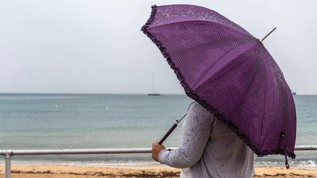 Una mujer contempla el mar mientras se protege de la lluvia con un paraguas. CATI CLADERA