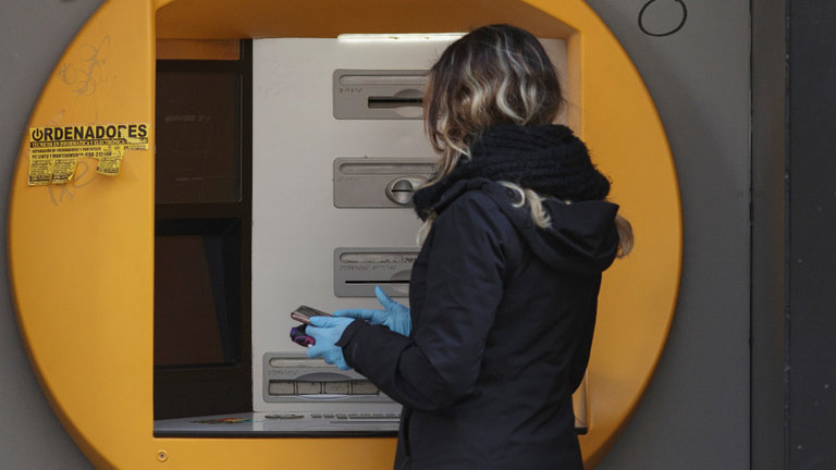 Una mujer saca dinero de un cajero con guantes como prevención ante el avance del coronavirus. EUROPA PRESS