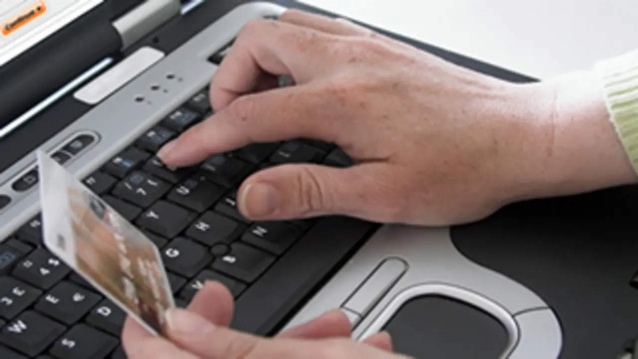 Un usuario escribe en un teclado y sostiene una tarjeta bancaria