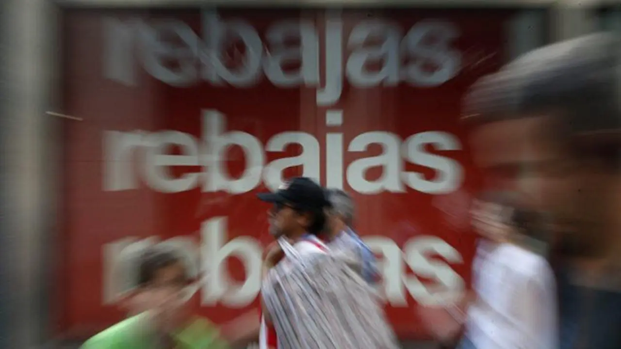 Varios viandantes pasan junto a un cartel de rebajas de un centro comercial en Madrid en el primer día de la campaña de verano. EP