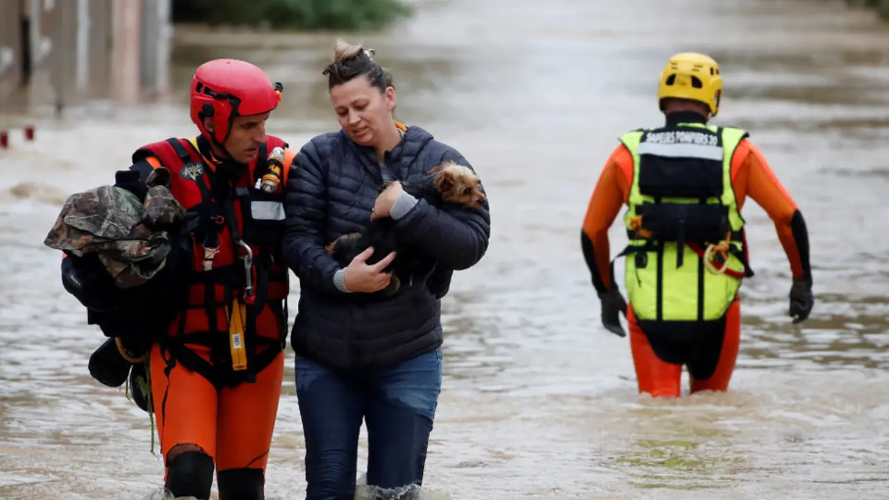 Un bombero ayuda a una mujer y a su perro a caminar por una calle anegada. GUILLAUME HORCAJUELO (Efe)
