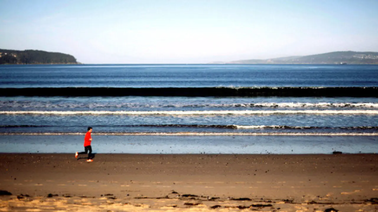Unha persoa corre pola Praia Grande de Miño durante unha soleada xornada. CABALAR