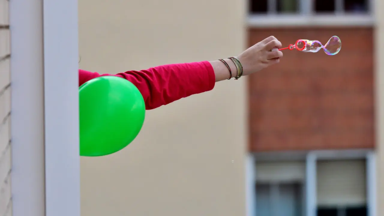 Una niña lanza pompas de jabón desde su casa durante el confinamiento. EFE