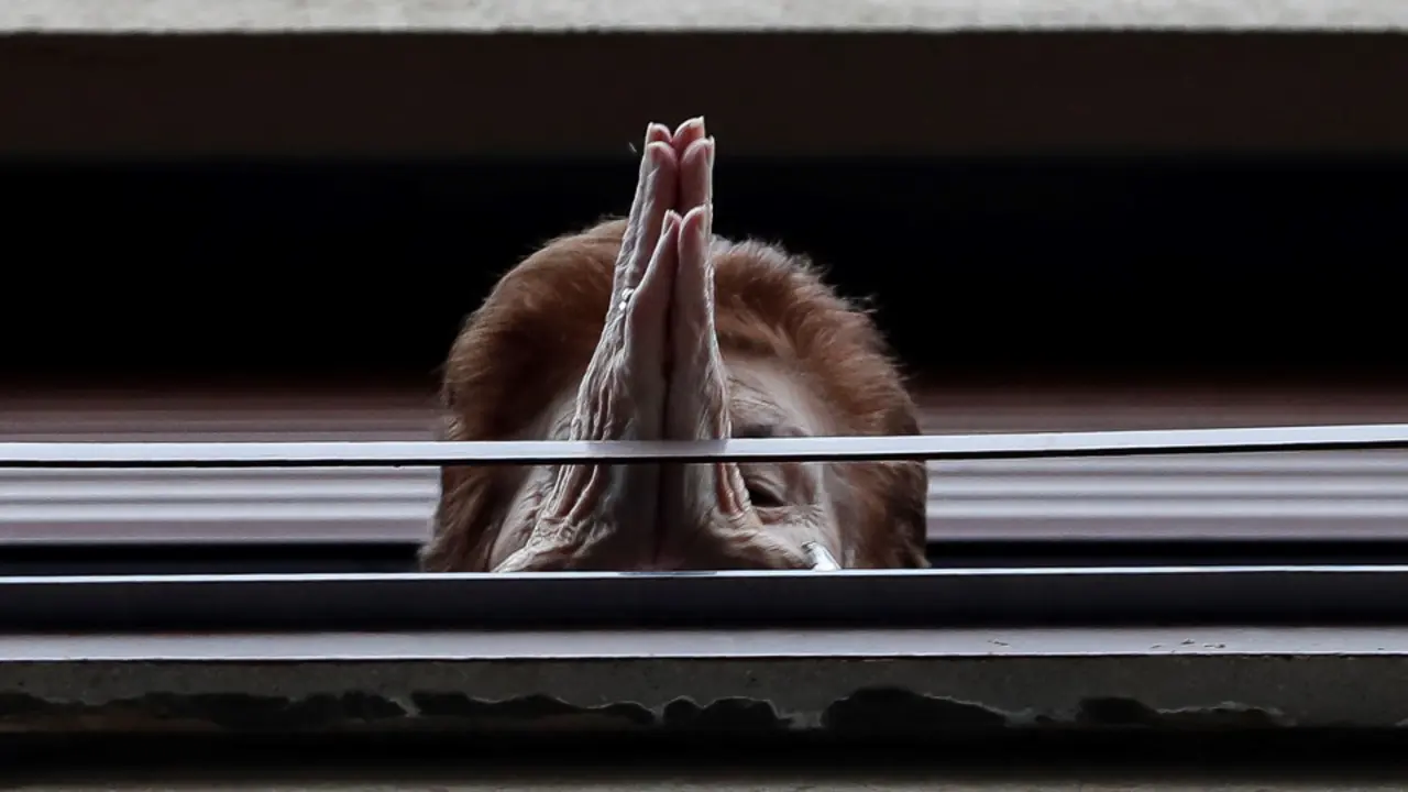 Una mujer mayor se asoma a la ventana durante el confinamiento. EFE