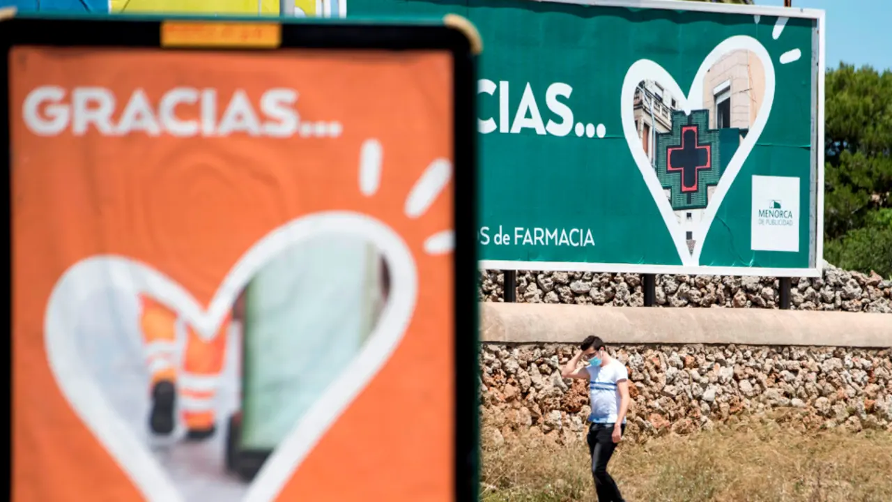 Un joven pasa ante una valla publicitaria en la que se agradece el esfuerzo de los servicios esenciales durante la pandemia de la Covid-19. DAVID ARQUIMBAU (EFE)