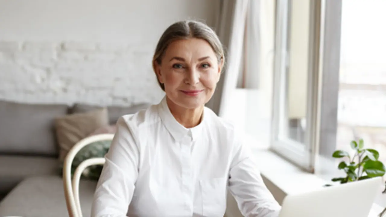 Portrait of happy skilled middle aged woman life coach, business consultant, psychologist or medical advisor smiling joyfully at camera, working on laptop, enjoying her job, helping people online