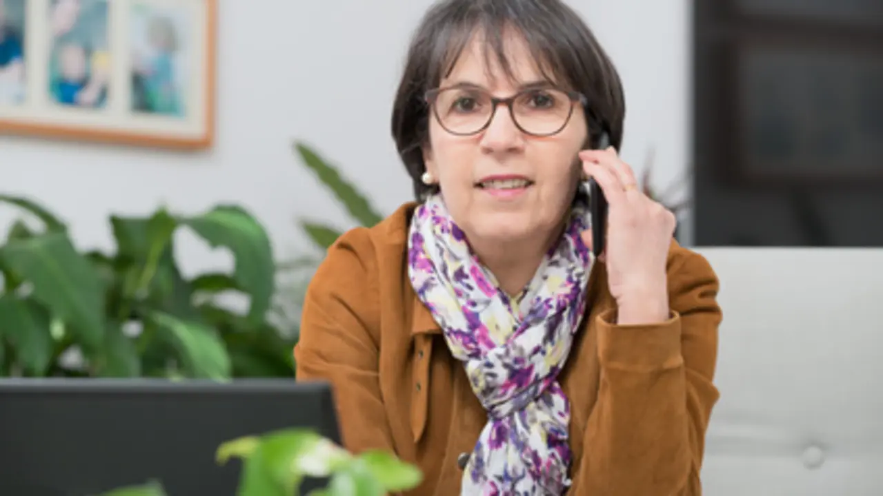 charming mature woman with brown jacket talking on phone at home
