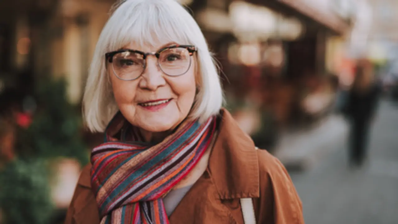 Portrait of stylish old lady in coat looking at camera and smiling. Street on blurred background