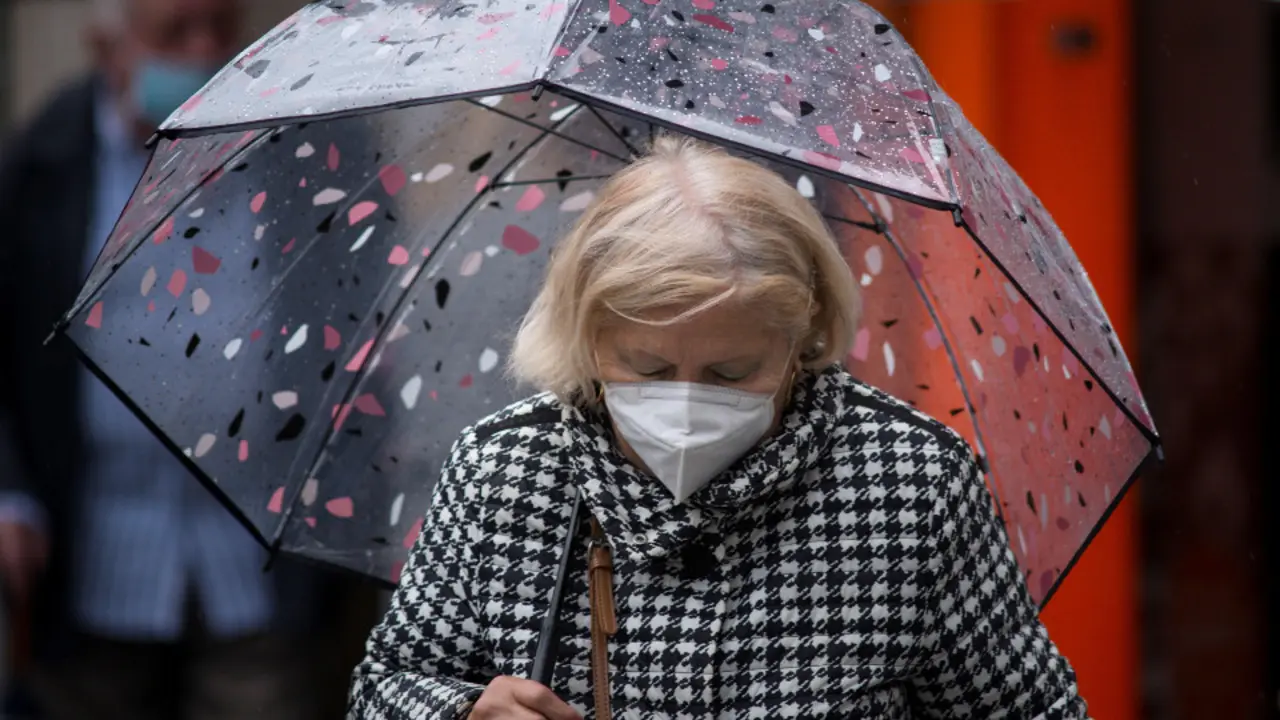 Una mujer con mascarilla y paraguas. EFE