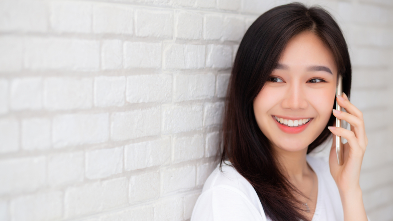 Beautiful of portrait young asian woman talk smart phone and smile standing on cement brick background, freelance female calling telephone, communication of mobile concept.