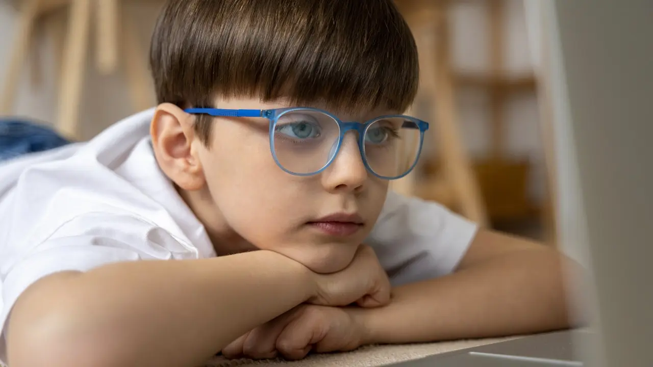 Un niño con gafas mirando la pantalla del ordenador. FREEPIK