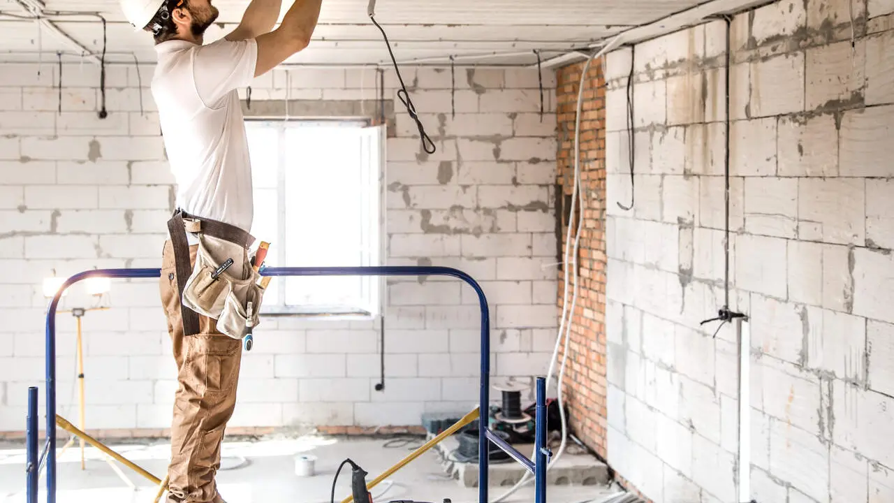 Electrician installer with a tool in his hands, working with cable on the construction site. Repair and handyman concept. House and house reconstruction.