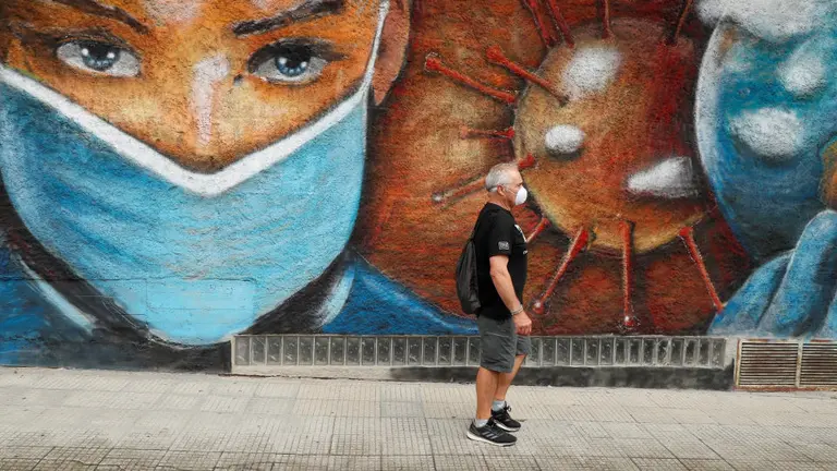 Un home cami&ntilde;a xunto a un mural en homenaxe aos sanitarios que loitaron contra o coronavirus nunha r&uacute;a de Melide. EFE/ Eliseo Trigo